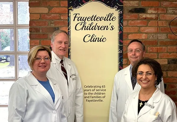 The doctors of Fayetteville Children’s Clinic beside a banner celebrating 65 years of service