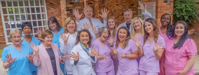 Clinic staff waving in front of the white-columned portico of the building